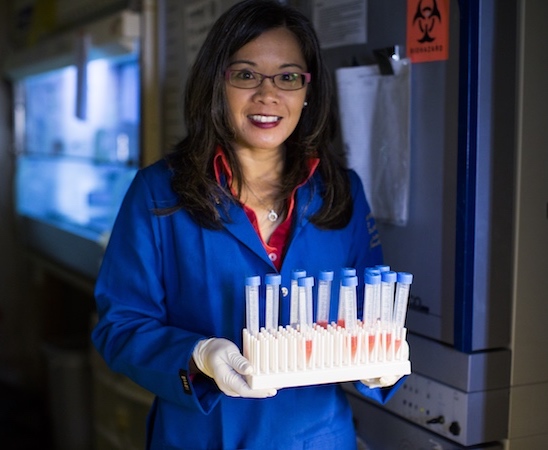 A woman in a blue lab coat holding a rack of test tubes.